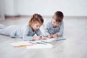 Children lie on the floor in pajamas and draw with pencils. Cute child painting by pencils