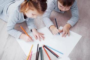 Children lie on the floor in pajamas and draw with pencils. Cute child painting by pencils.Hand of child girl and boy draw and paint with crayon. Close up view photo