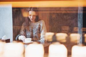 Mujer sonriente en la cafetería mediante teléfono móvil y mensajes de texto en las redes sociales, sentada sola foto