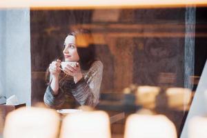 Mujer sonriente en la cafetería mediante teléfono móvil y mensajes de texto en las redes sociales, sentada sola