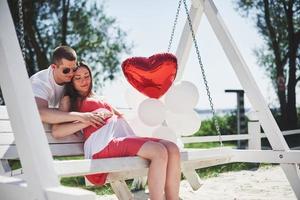 waiting baby. pregnant woman with beloved husband sit on a bench. Husband hand embraces a round belly wife. Parenthood. pregnant woman in a white dress in cherry with a red bow. close-up. nine months photo