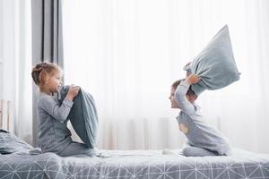 niño y niña organizaron una pelea de almohadas en la cama del dormitorio. los niños traviesos se golpean las almohadas. les gusta ese tipo de juego foto