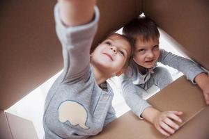 dos niños pequeños, niño y niña, abriendo una caja de cartón y trepando por el medio. los niños se divierten