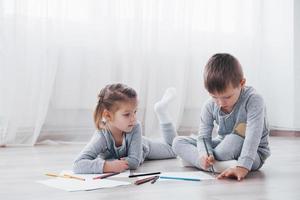 los niños se acuestan en el suelo en pijama y dibujan con lápices. lindo niño pintando con lápices foto