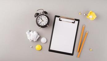 Blank paper on clipboard, white alarm clock and stationery top view on gray background