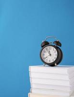 Black alarm clock on stack of books on blue background, mockup design photo