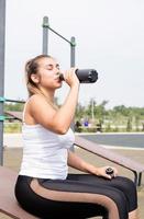 Mujer feliz trabajando en el campo de deportes en un día soleado de verano, bebiendo agua de la botella