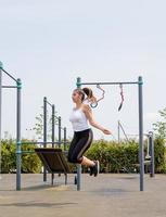 Happy woman working out on the sports ground in sunny summer day jumping rope photo