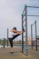 Happy woman working out on the sports ground in sunny summer day stretching her legs photo