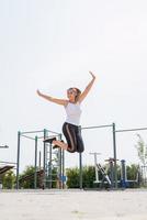 Happy woman jumping on the sports ground in sunny summer day, raising arms up, enjoying the sun photo