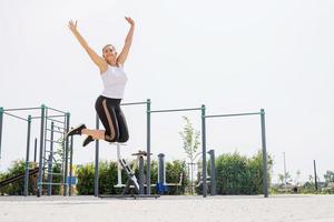 Happy woman jumping on the sports ground in sunny summer day, raising arms up, enjoying the sun photo