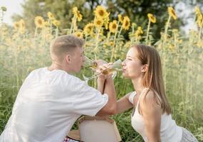 Young couple having picnic on sunflower field at sunset