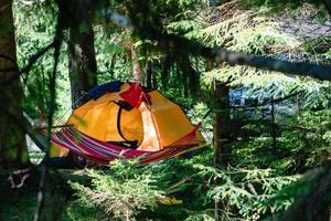 Carpa amarilla en el bosque con hamaca y coche en el fondo foto