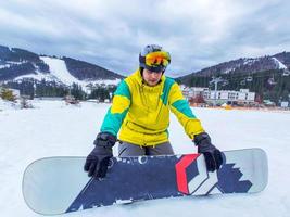 Hombre con tabla de snowboard sentado en la colina nevada foto