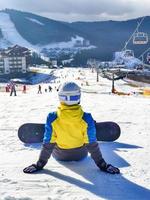 Woman sitting with snowboard on hill enjoying the view photo