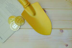 Close up of gold bitcoin coins on bank passbook with a golden shovel on wooden table photo