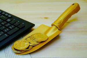 Close up of gold bitcoin coins on bank passbook with a golden shovel on wooden table photo