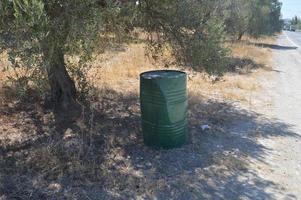 A green metal barrel stands in the shade of a tree photo