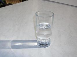 A transparent glass with water stands on a white table photo