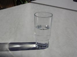 A transparent glass with water stands on a white table photo