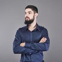 Young handsome man with a beard leaning against grey wall with arms crossed. photo