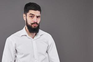 hipster con cara seria. sentimiento y emociones. chico o hombre barbudo sobre fondo gris. peluquería de moda y belleza. hombre con barba larga y bigote, espacio de copia foto