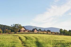 Village houses on hills with green meadows in summer day. House of shepherds in mountains in carpathian photo