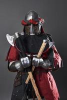 Medieval knight on grey background. Portrait of brutal dirty face warrior with chain mail armour red and black clothes and battle axe photo