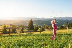 Cute happy little baby girl play outdoors in the early morning in the lawn and admiring mountains view. Copy space for your text photo