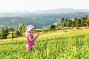 Cute happy little baby girl play outdoors in the early morning in the lawn and admiring mountains view. Copy space for your text photo