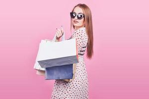 retrato, de, joven, feliz, mujer sonriente, con, bolsas de compras, en, el, fondo rosa