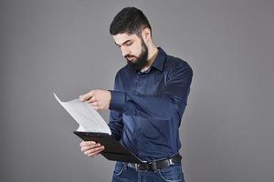 Concentrated young attractive businessman in blue shirt planning and writing in clipboard photo