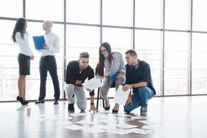 Planning strategy together. Business team looking at papers on floor with manager pointing to one idea. Cooperation corporate achievement. Planning design draw. Teamwork concept photo