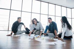 Planning strategy together. Business team looking at papers on floor with manager pointing to one idea. Cooperation corporate achievement. Planning design draw. Teamwork concept photo