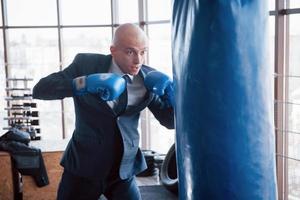 un hombre de negocios calvo enojado golpea una pera de boxeo en el gimnasio. concepto de manejo de la ira