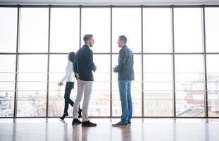 Dos hombres de negocios enfrascados en una discusión juntos mientras están parados en una sala de juntas de oficina con ventanas que dan a la ciudad