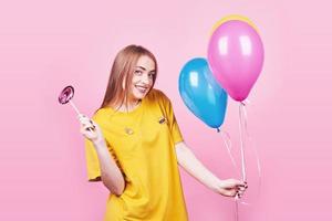 Cute funny girl portrait holds an air colorful balloons and lollipop smiling on pink background. Beautiful multicultural Caucasian girl smiling happy photo