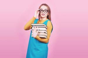 Feliz linda chica en vasos sosteniendo en las manos un montón de libros aislado sobre fondo de color rosa colorido foto