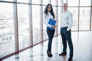 Businessman and business woman studying a chart on the plate and paper documents at the window on the background of the city office on a high floor photo