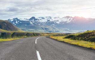Travel to Iceland. road in a bright sunny mountain landscape. Vatna volcano covered with snow and ice on tne background