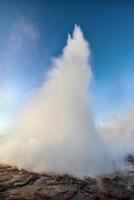 Erupción del géiser strokkur en islandia. colores fantásticos brillan a través del vapor. hermosas nubes rosadas en un cielo azul foto