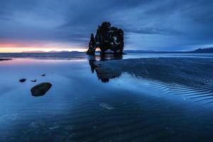 es una roca espectacular en el mar en la costa norte de islandia. las leyendas dicen que es un troll petrificado. en esta foto hvitserkur se refleja en el agua del mar después de la puesta de sol de medianoche
