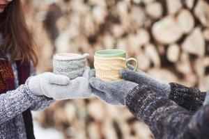 Couple hands in mittens take a mugs with hot tea in winter park photo