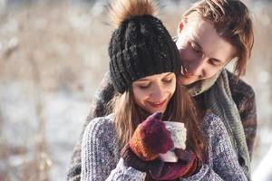 Photo of happy man and pretty woman with cups outdoor in winter. Winter holiday and vacation. Christmas couple of happy man and woman drink hot wine. Couple in love