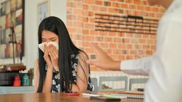 Una mujer joven usa un pañuelo de papel para cubrirse la boca y estornuda en un café. Está en riesgo de propagar el virus covid-19. foto