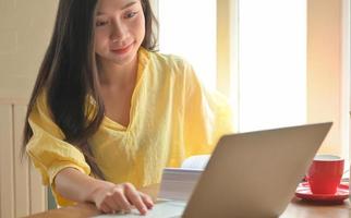 Asian teenage female student search for information from laptop and take notes. She prepares for university entrance exam. photo