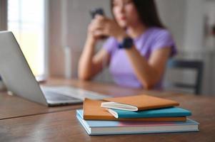 A notebook with a laptop on the table and a young woman using a smartphone on the back. photo