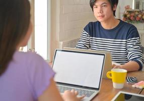 joven estudiante usa una computadora portátil y aconseja a un estudiante sentado enfrente. están estudiando en línea en casa.