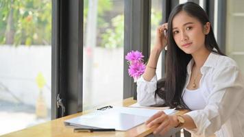 Asian girl student with study materials in a shared workspace,She looking at the camera and smiling. photo