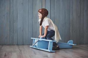 Happy kid in pilot hat playing with wooden airplane against. Childhood. Fantasy, imagination. Holiday photo